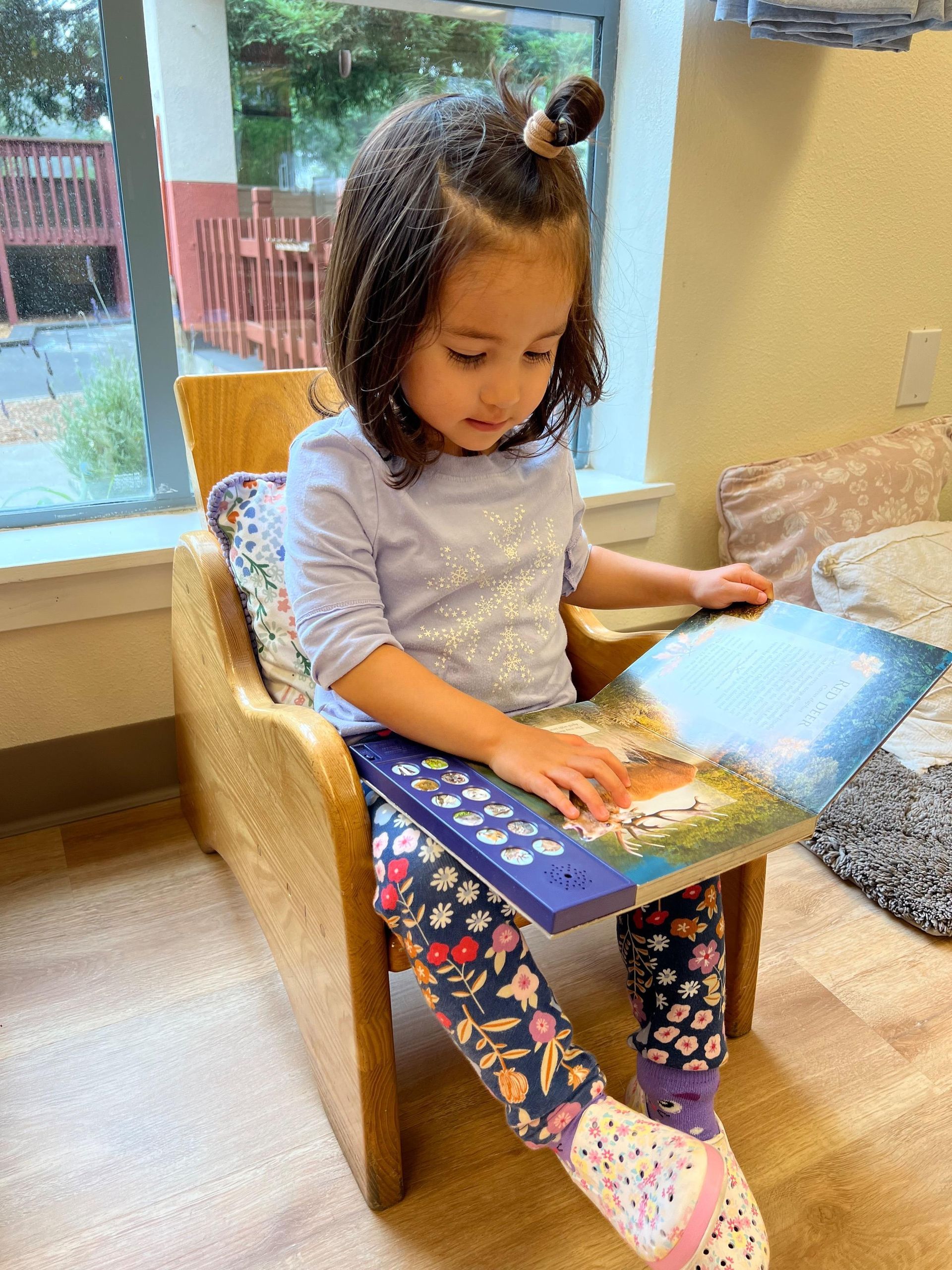 A Montessori child is sitting in a chair reading a book.