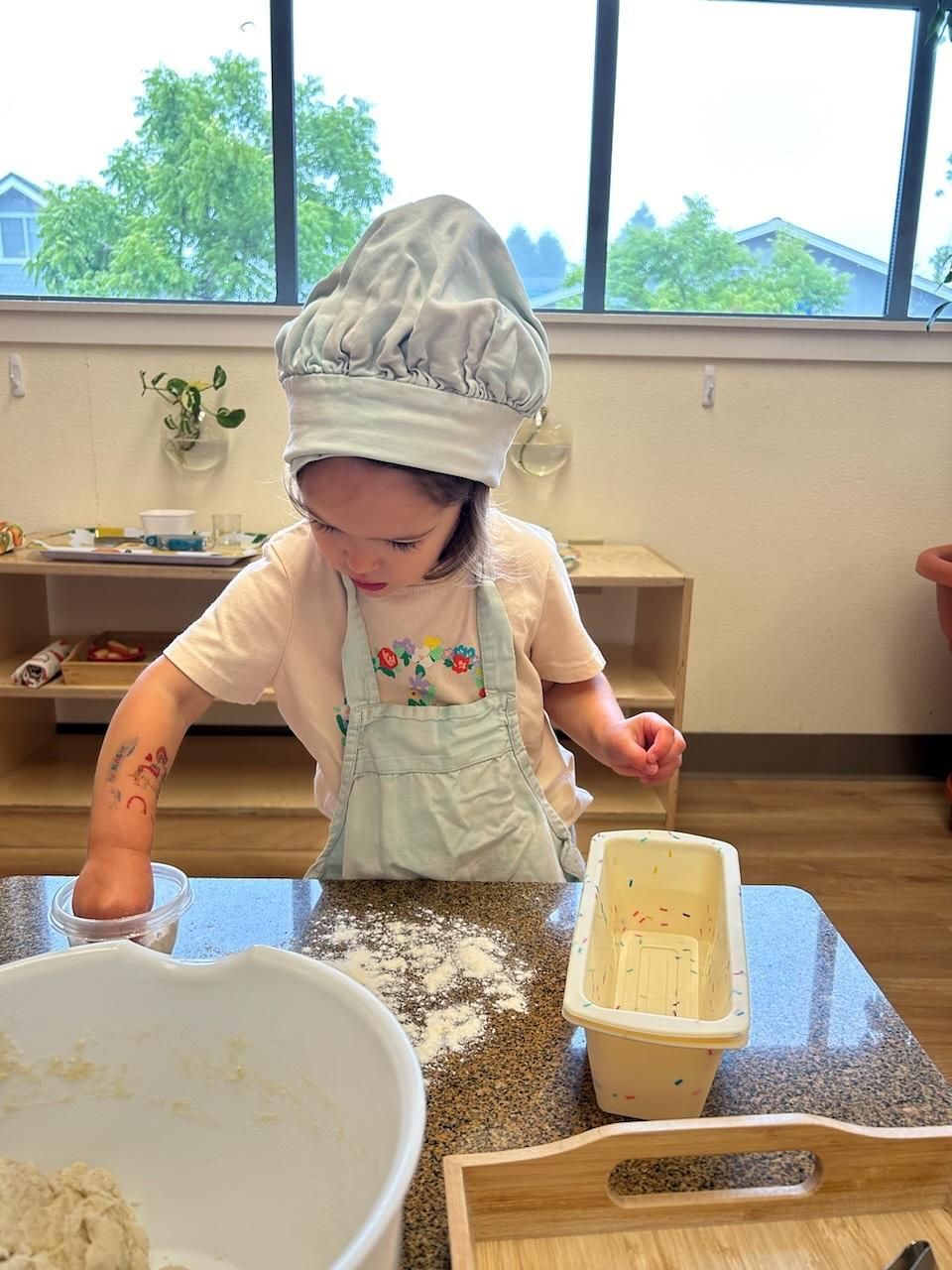 A Montessori child is mixing ingredients in a bowl with a wooden spoon.