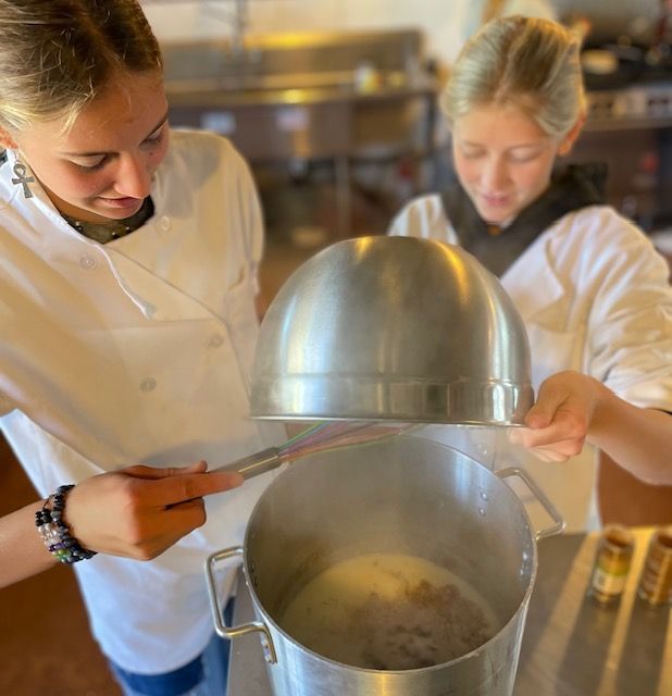 Two Montessori children in white aprons are cooking in a pot