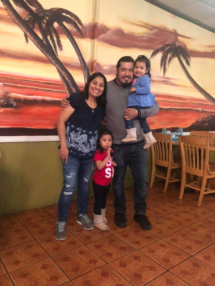 A family posing for a picture in front of a painting of palm trees.