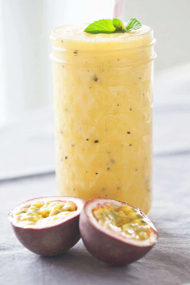 A smoothie in a mason jar next to two passion fruits.