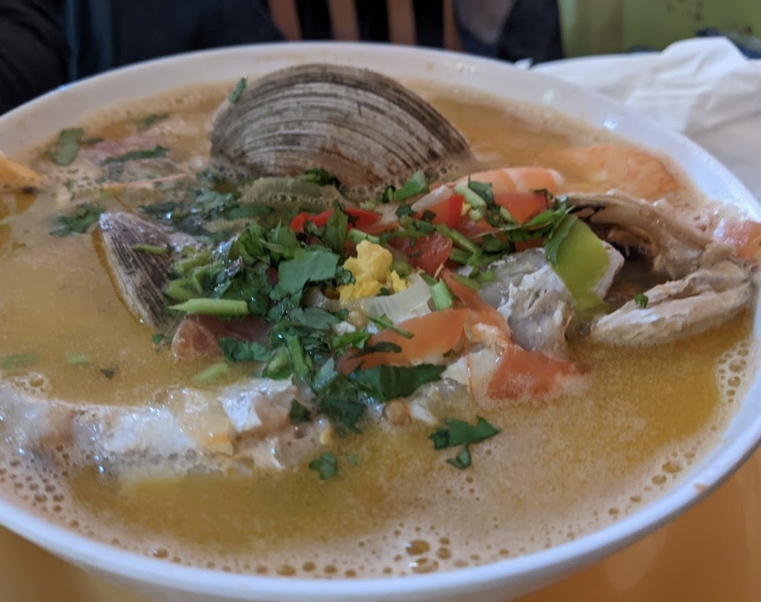 A bowl of soup with seafood and vegetables on a table.