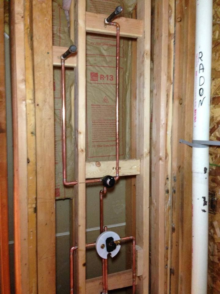 A bathroom under construction with copper pipes and a white pipe.