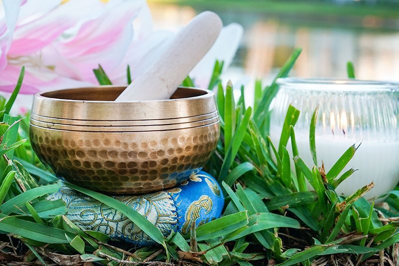 a singing bowl is sitting on top of a rock in the grass next to a candle .