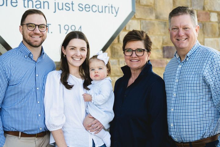 A family is posing for a picture in front of a sign that says `` more than just security ''.