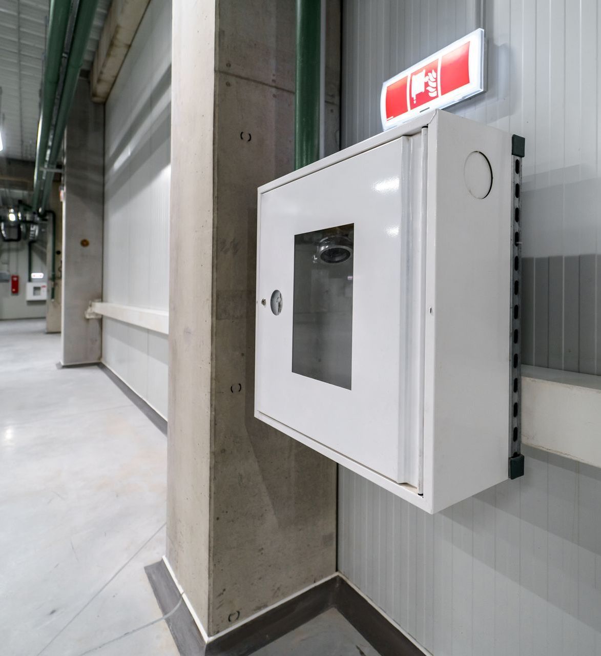 A white fire hydrant box is hanging on a wall in a building.