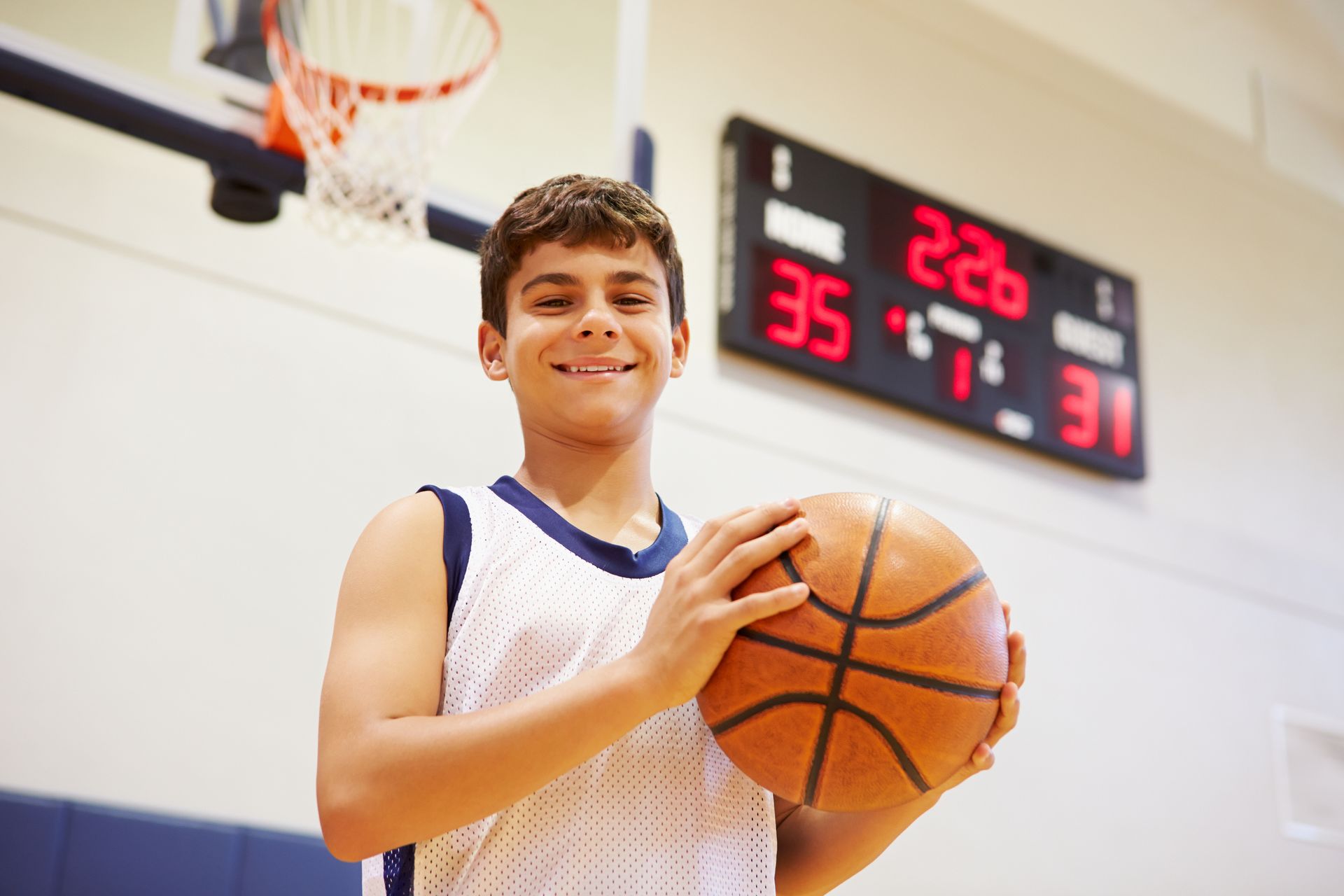 Smiling basketball player holding a ball on the court, scoreboard in the background.