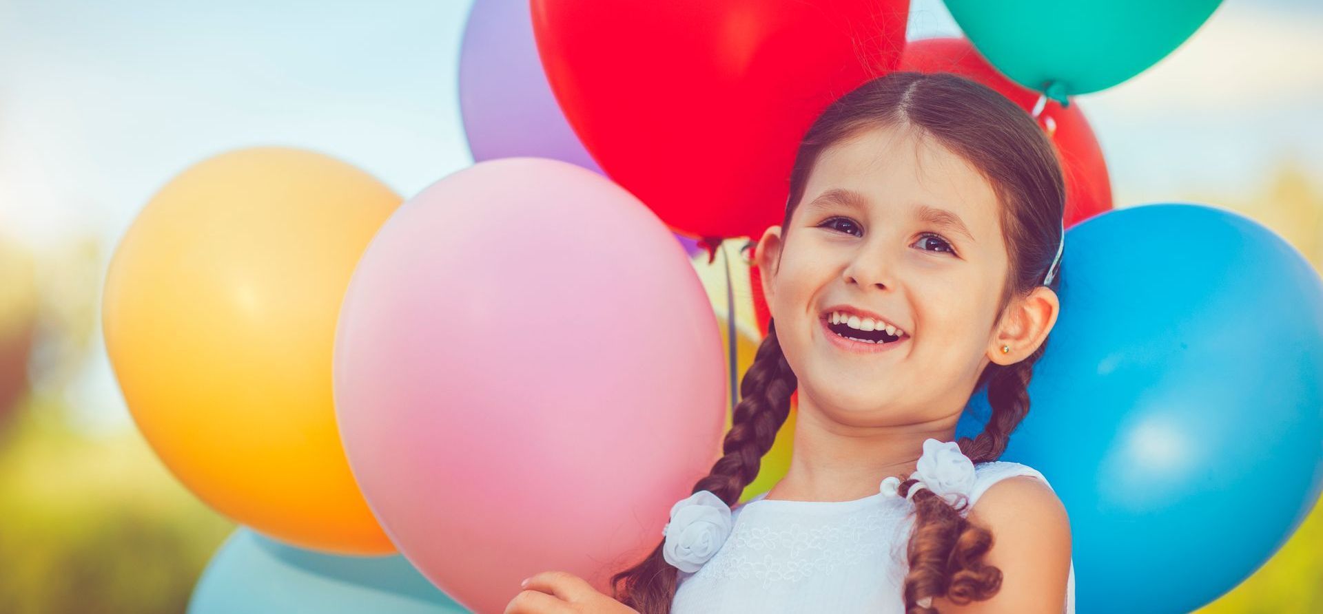 Young girl, smiling and holding a bunch of colorful balloons.