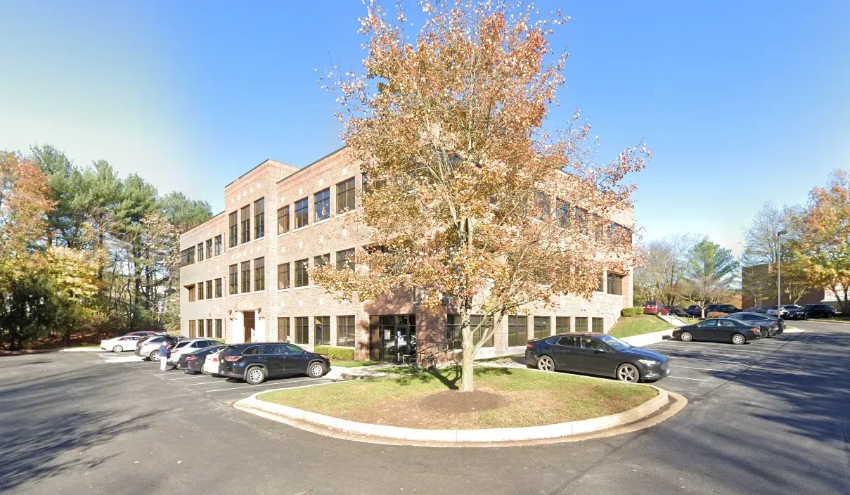Three-story brick building with a tree in front; cars parked along the side.