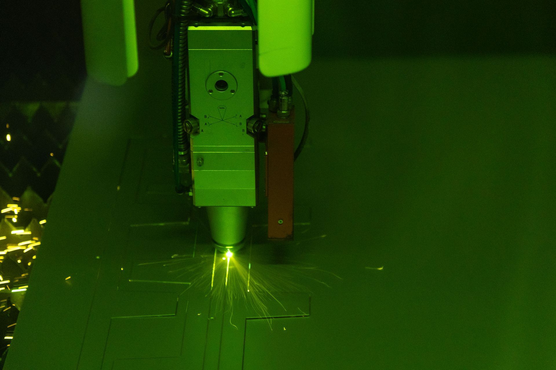 Laser cutter cutting metal sheet; sparks and green light visible.