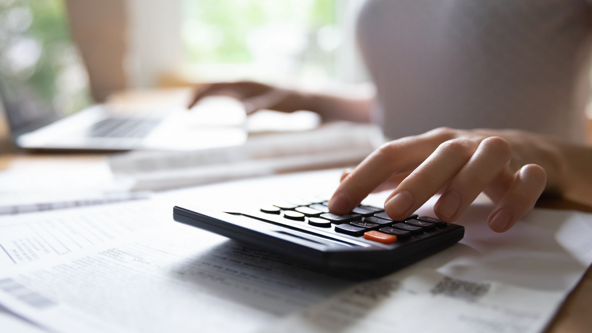 Una persona está usando una calculadora mientras escribe en una computadora portátil.