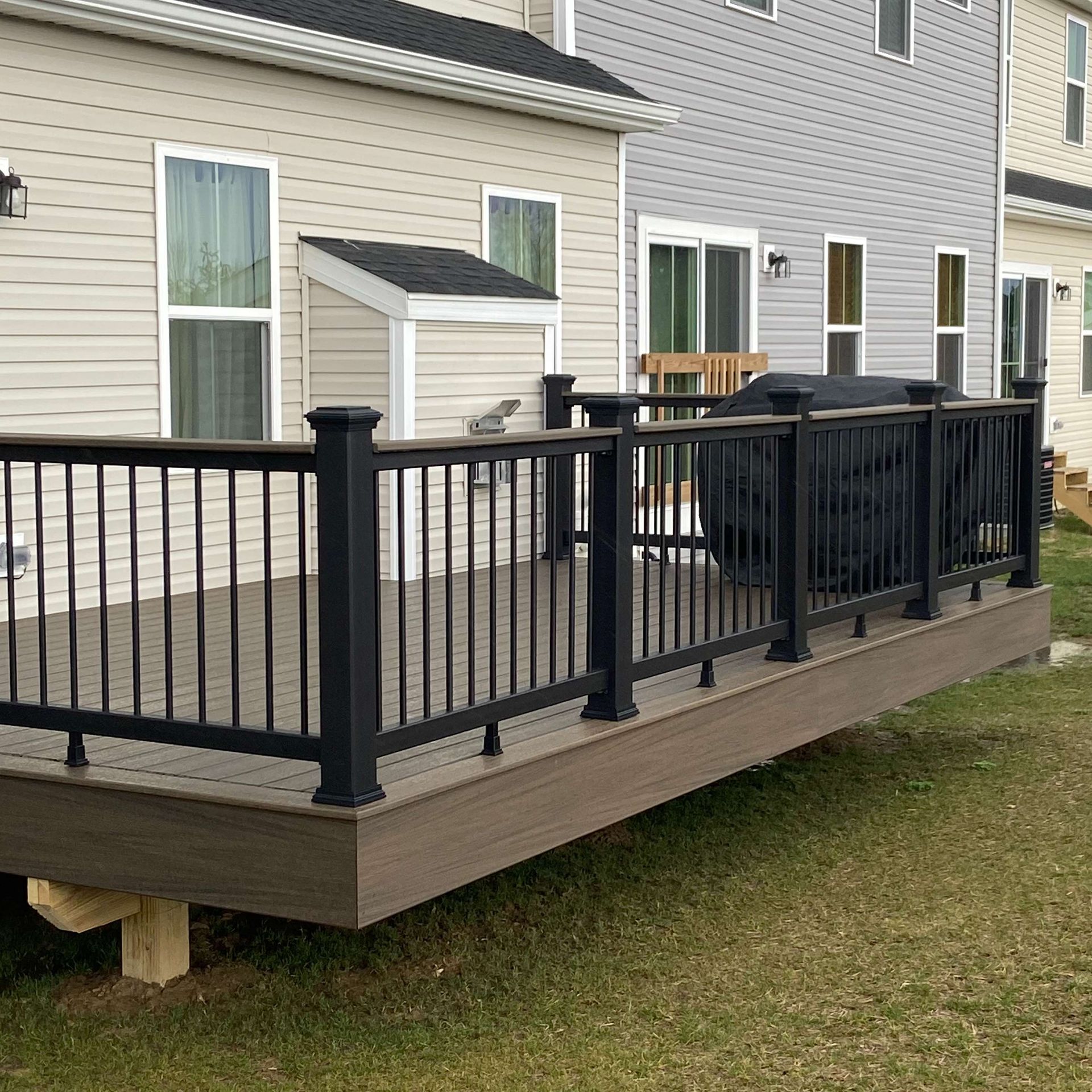 A deck with a black railing is in front of a house.
