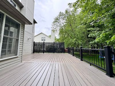 A large wooden deck with a black railing in front of a house.