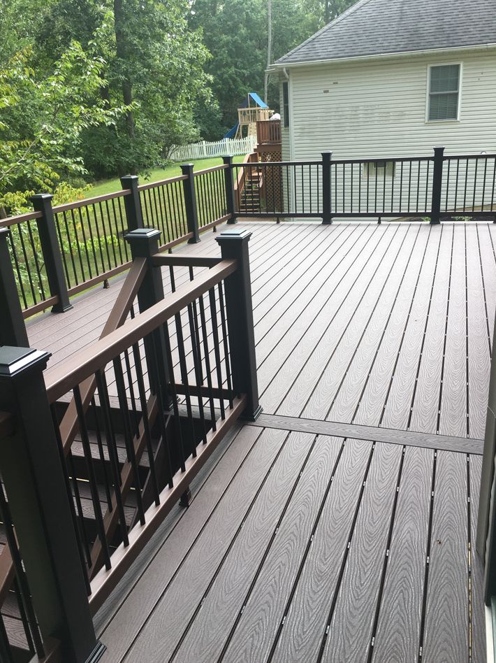 A wooden deck with stairs and a black railing in front of a house.