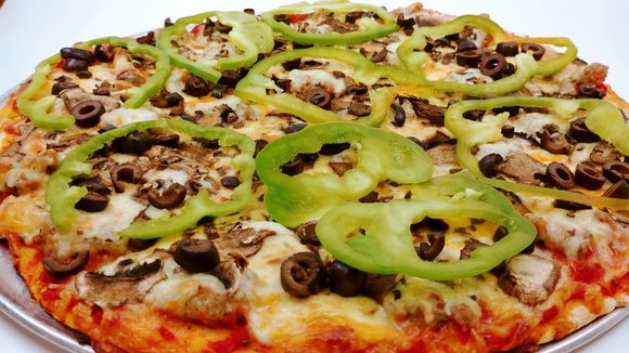 A pizza with peppers , olives , mushrooms and cheese on a pan.