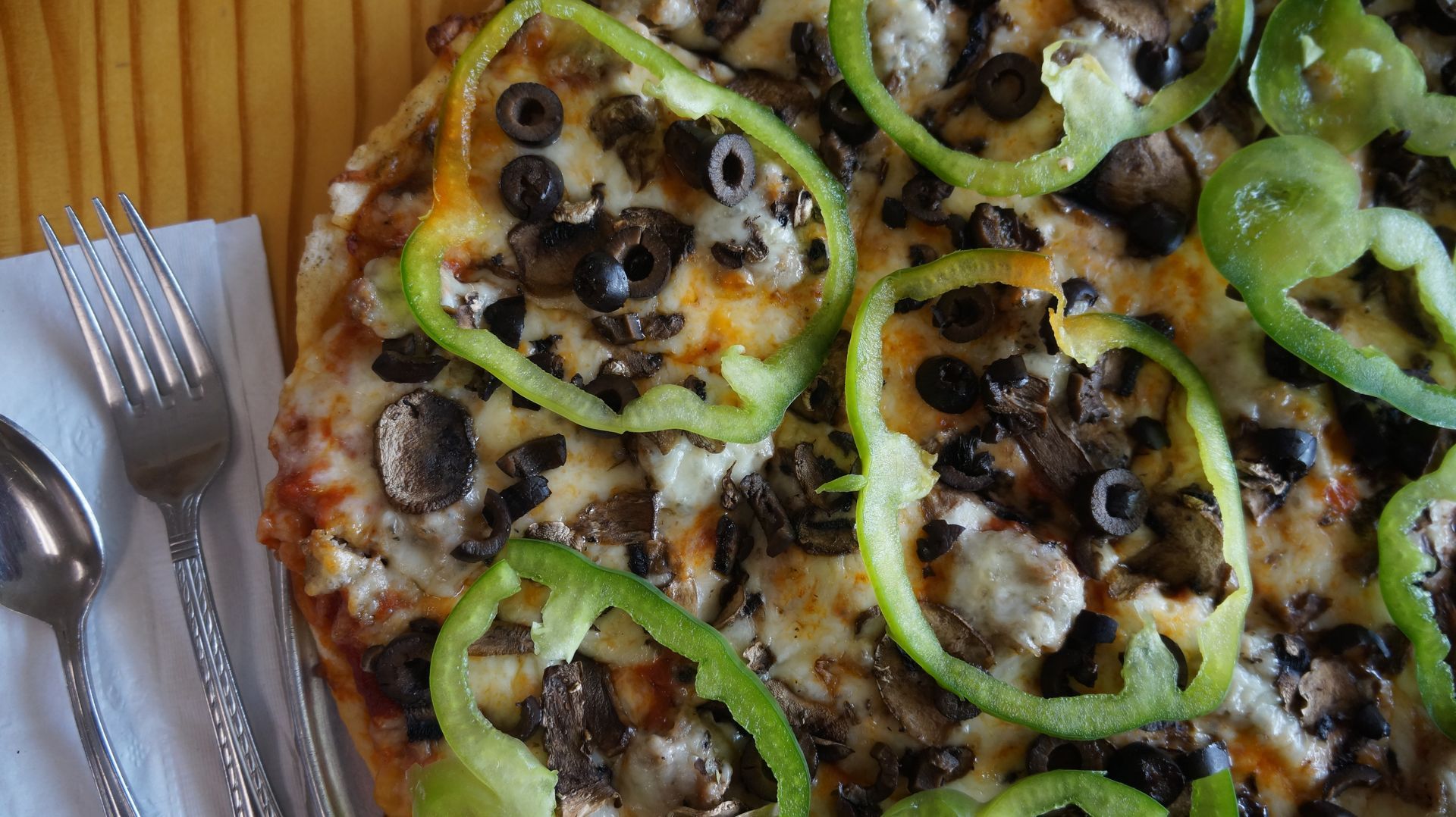 A pizza with peppers , olives , mushrooms and cheese on a wooden table.