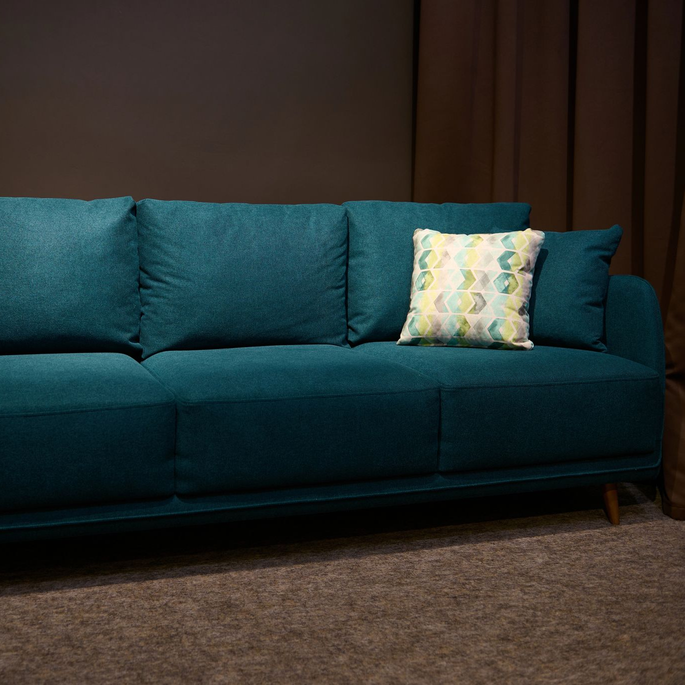 Divano color verde acqua con tre cuscini posteriori e cuscino decorativo decorato, su uno sfondo scuro.