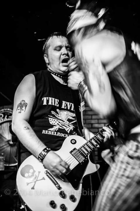 A man wearing a shirt that says the evil is playing a guitar