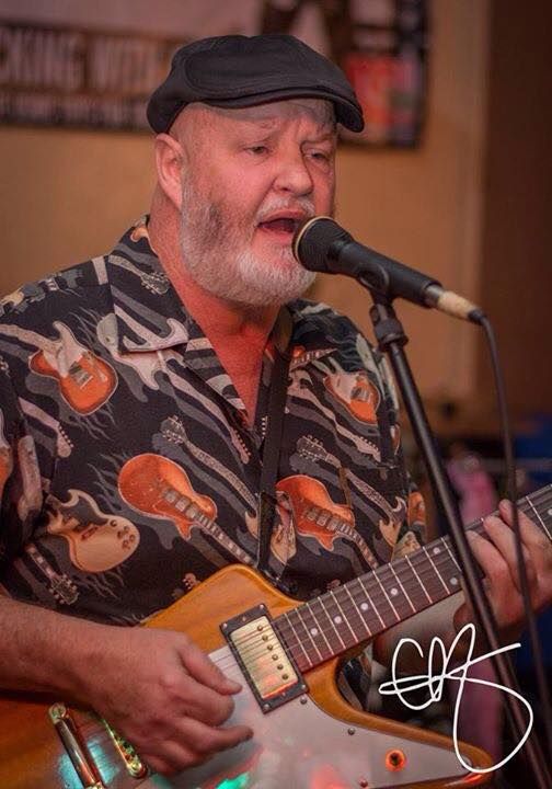 A man singing into a microphone while playing a guitar