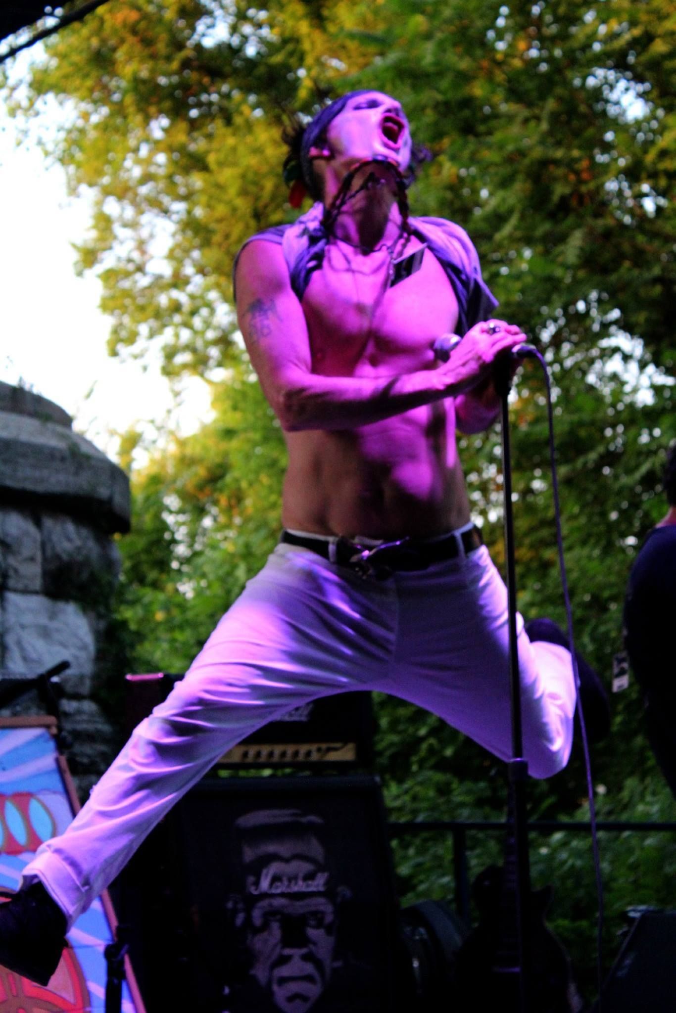 A shirtless man is jumping in the air while singing into a microphone.