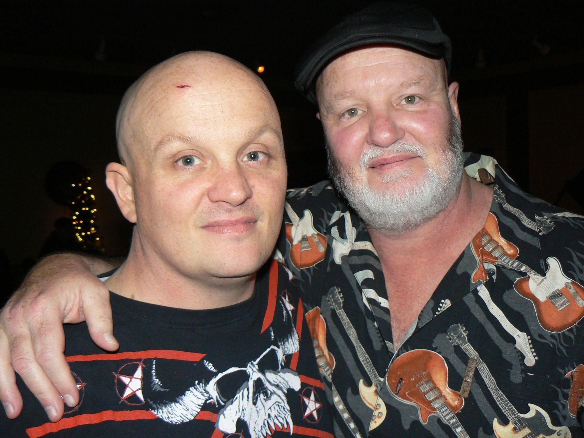 Two men posing for a picture with one wearing a shirt with guitars on it