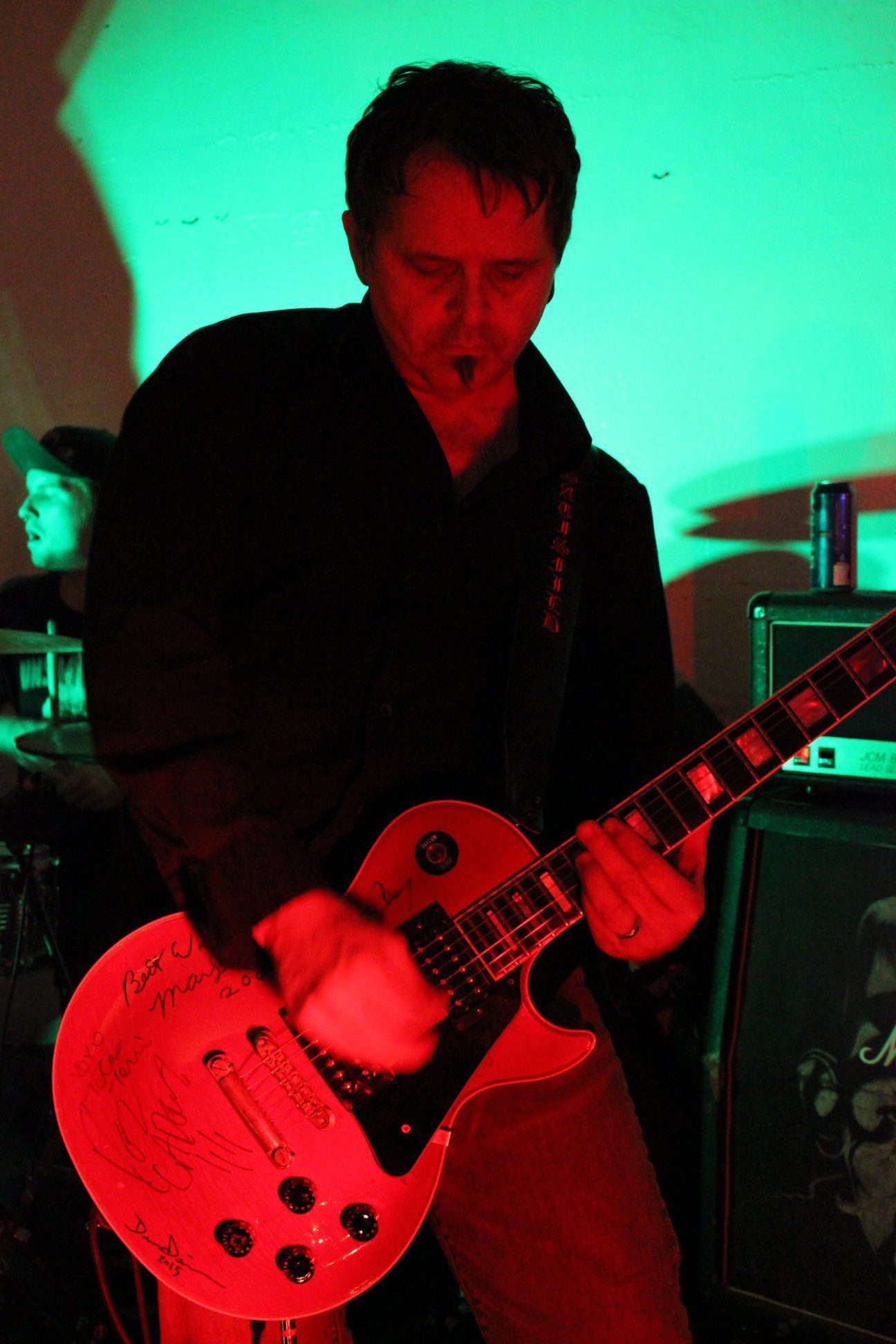 A man is playing a red guitar in a dark room