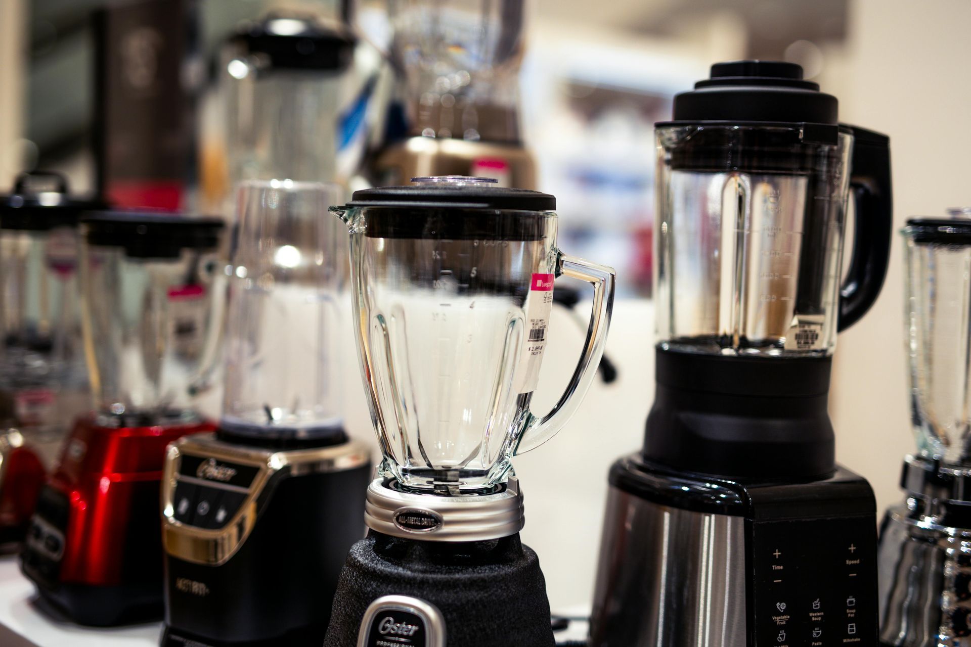 Various blenders on display, featuring glass and colored bases, in a store setting.