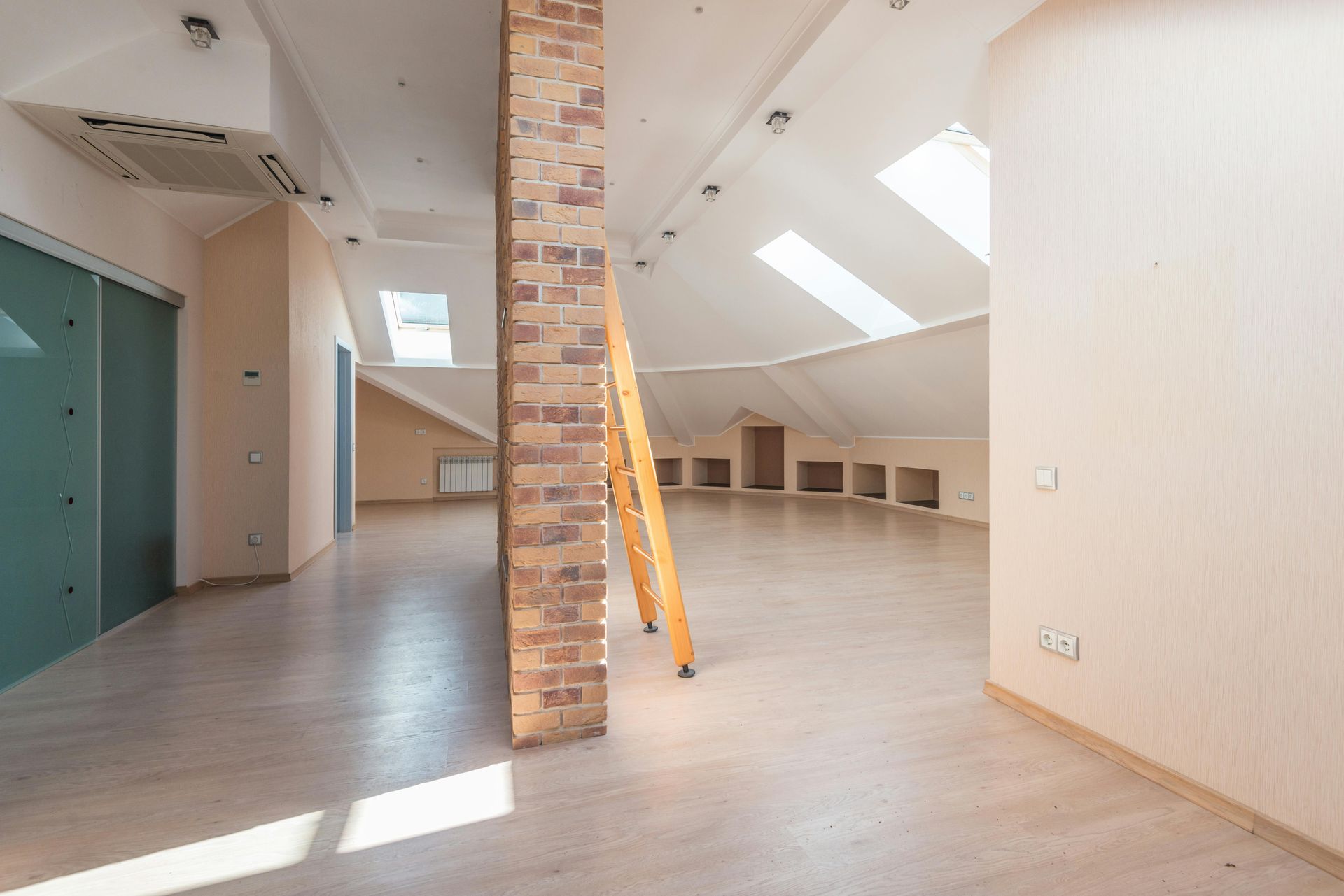 Empty, light-filled attic room with skylights, light wood floors, and exposed brick column.