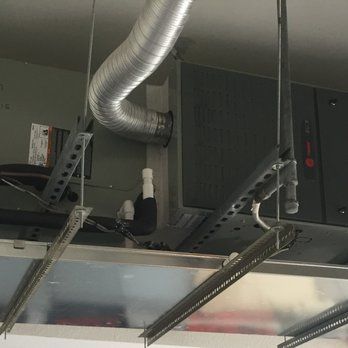 HVAC unit with flexible ductwork and hanging metal fixtures against a light-colored ceiling.