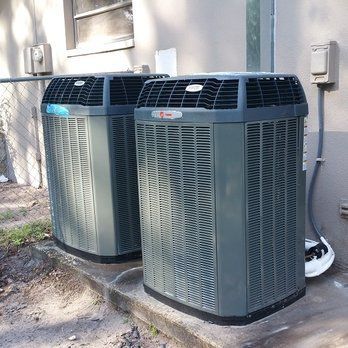 Two gray air conditioning units sitting on a concrete pad near a building.