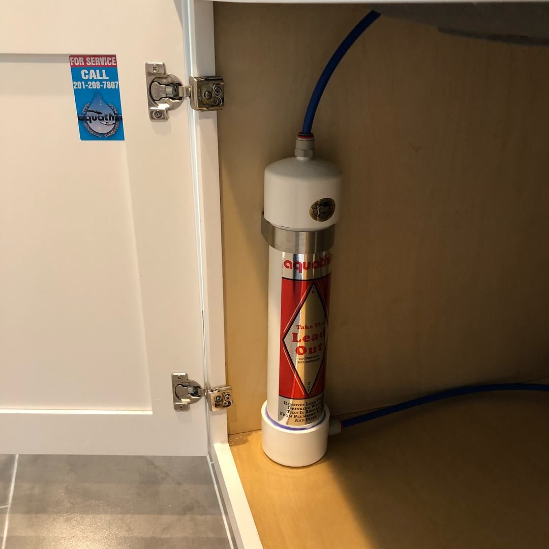Water filter installed under a white cabinet. Red and silver filter, blue tubing.