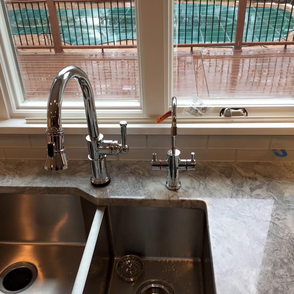 Stainless steel kitchen sink with two faucets against a white-framed window.