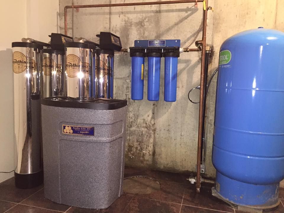 Water filtration system with tanks, filters, and pressure tank in a basement setting.