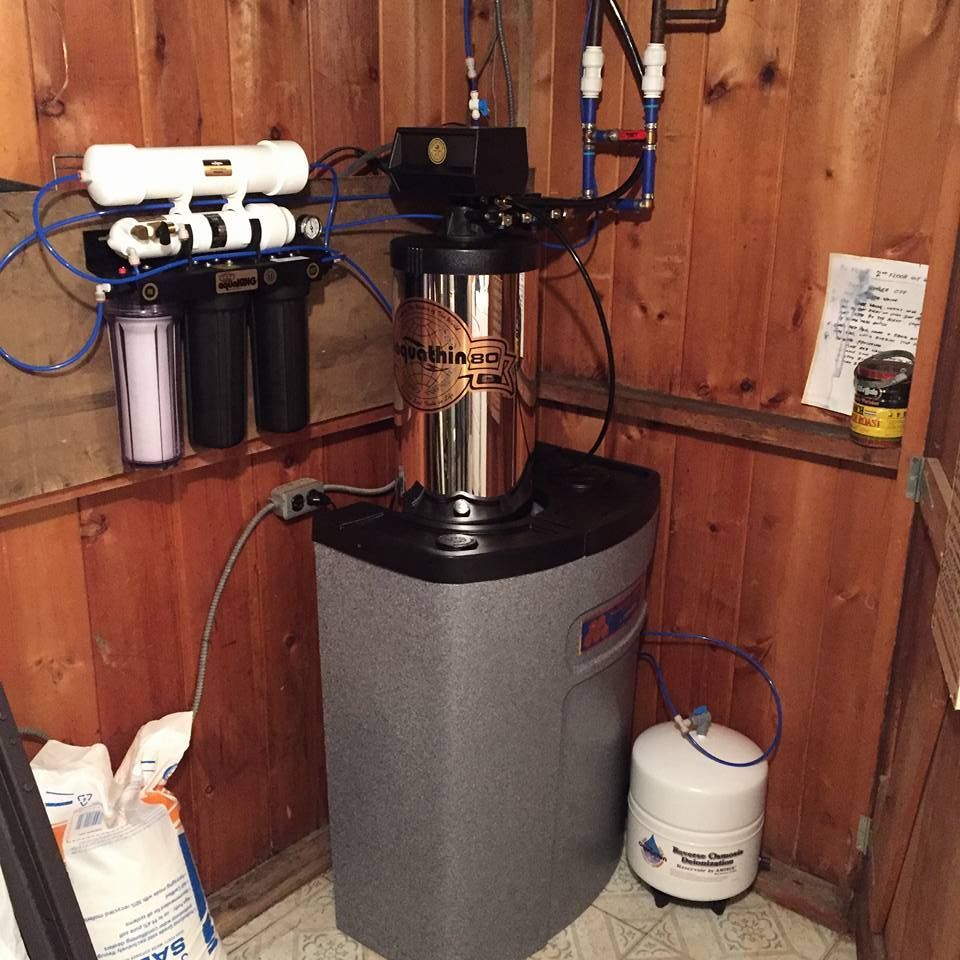 Water filtration system in wooden-paneled room: stainless steel tank, pre-filters, storage tank.