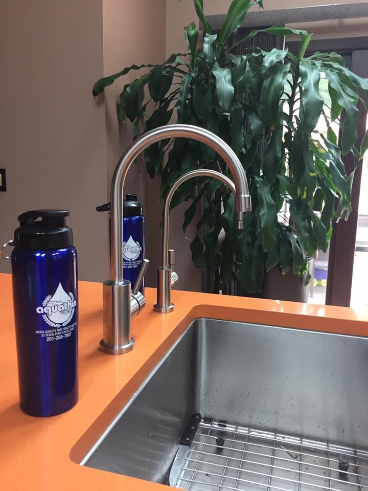 Blue water bottle next to a kitchen sink with a faucet on an orange countertop. Green plant in background.