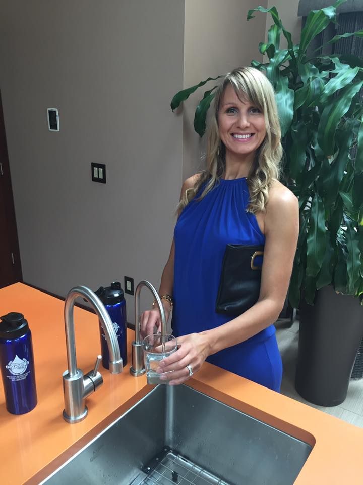 Woman in blue dress filling a glass with water from a sink in a modern kitchen.