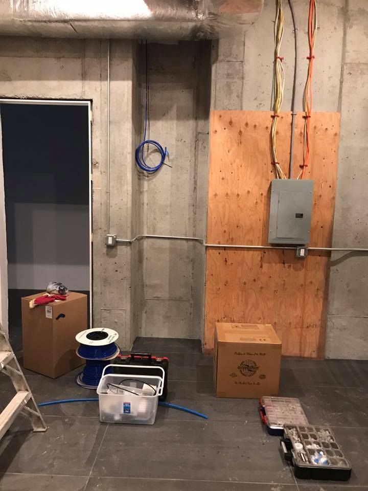 Construction site with electrical panel on plywood, wires, tools, and open doorway.
