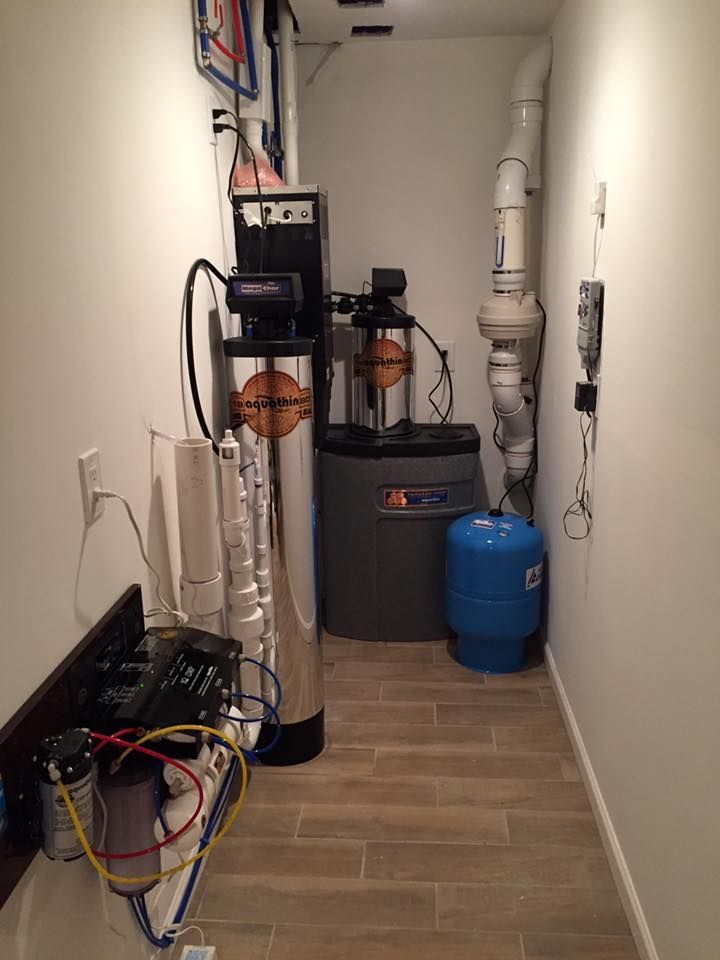 Water filtration and softening system in a narrow utility room with plumbing and tanks.