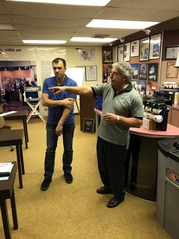 Man points, explaining something to another man in a business interior with equipment.