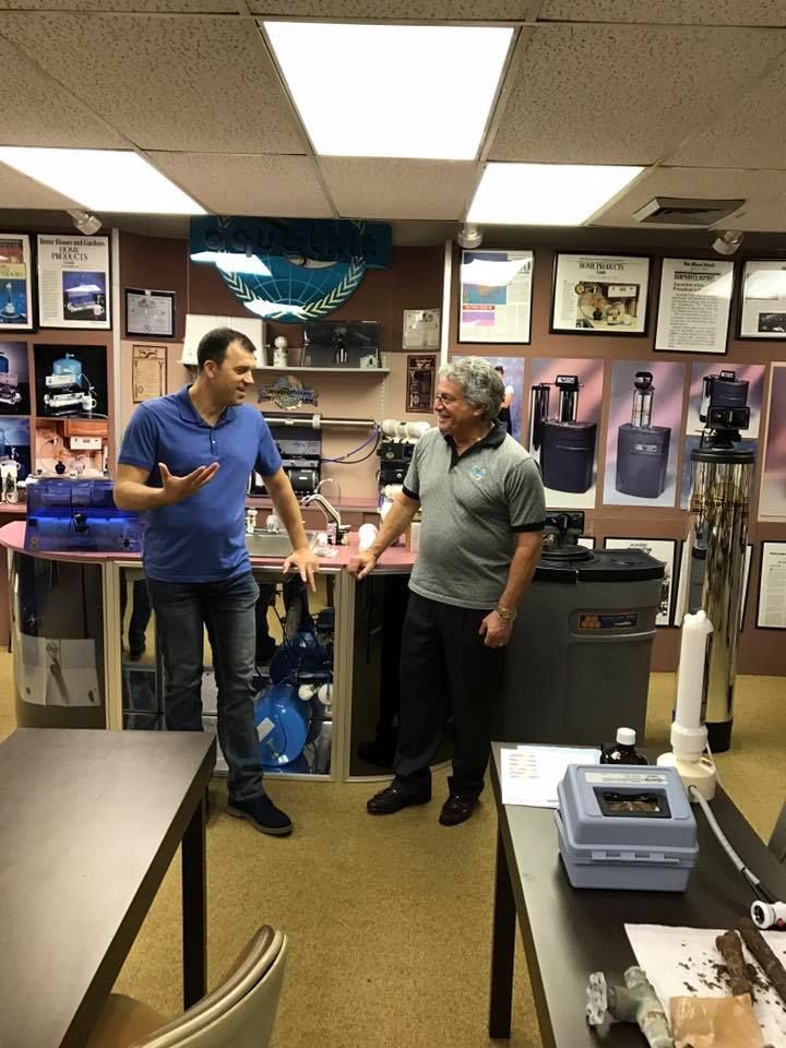 Two men conversing near water treatment equipment in an office setting.