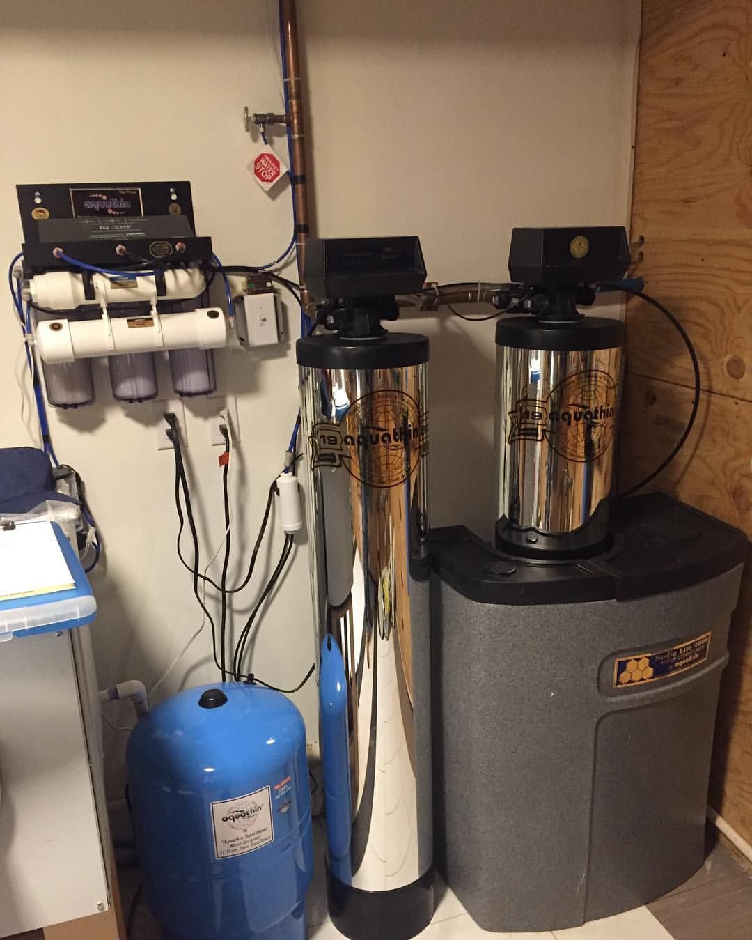 Water filtration system in a utility room. Includes tanks, filters, and a pressure tank.