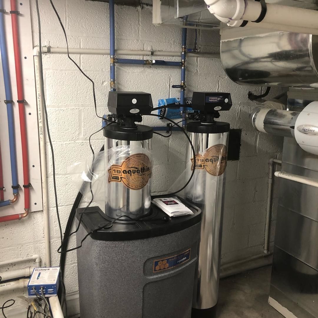 Water filtration system with two silver tanks, blue pipes, and a gray base, indoors.