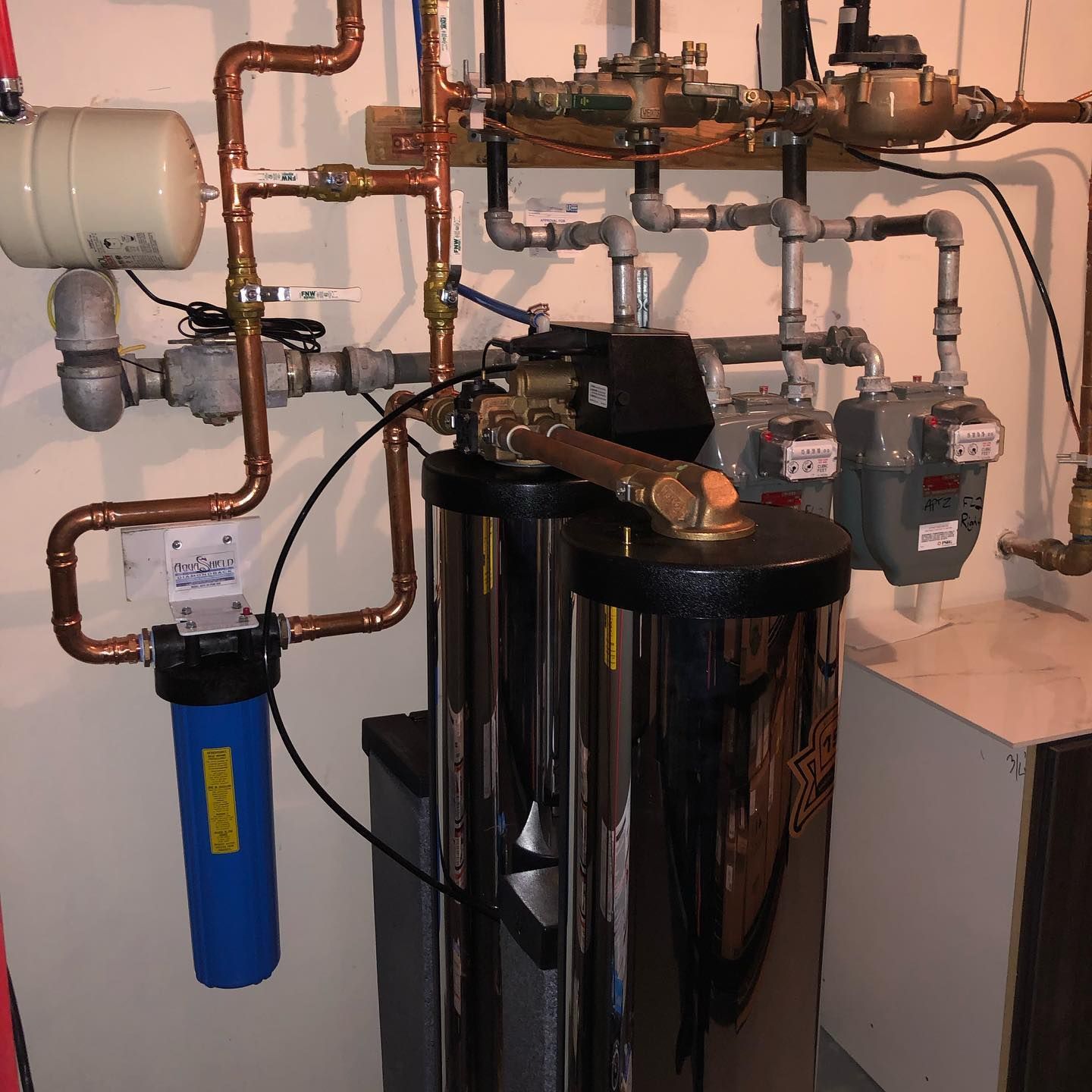 Plumbing system with copper pipes, a blue water filter, and two large stainless steel tanks.