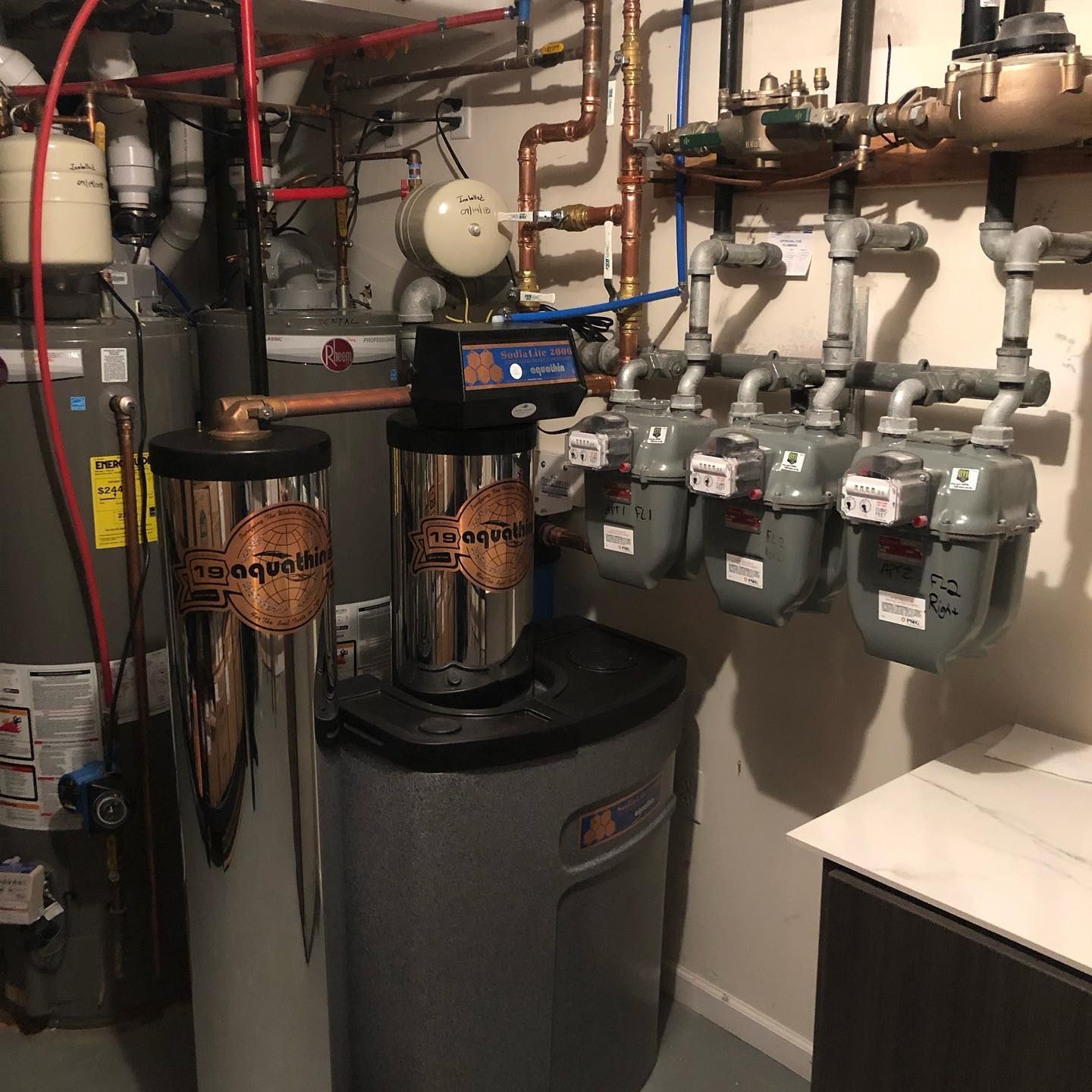 Plumbing and water treatment system in a basement, including tanks, meters, and pipes.