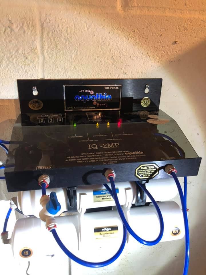 Water filtration system with black control panel and blue tubing on a brick wall.