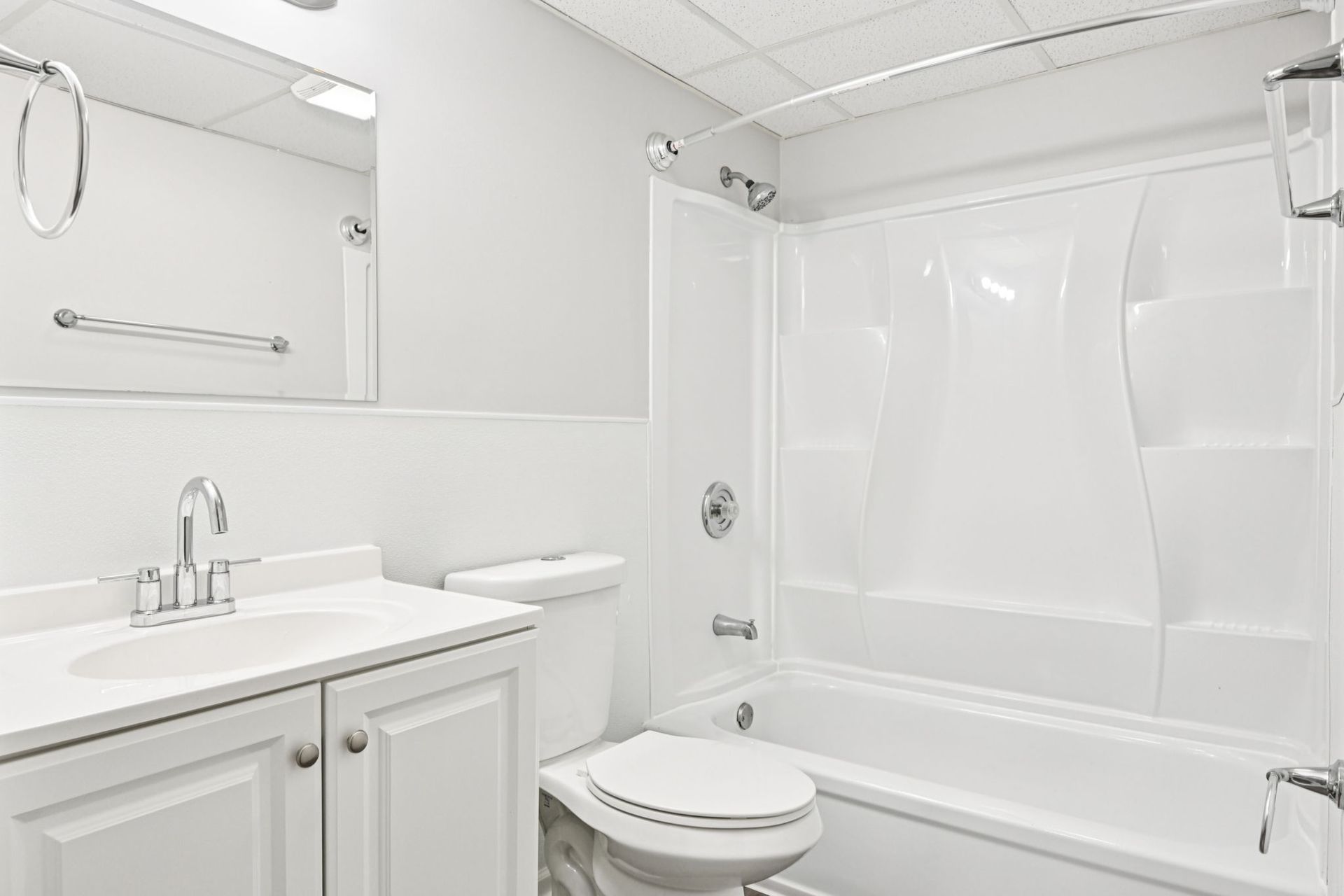 All-white bathroom with a vanity, toilet, and bathtub/shower combo.
