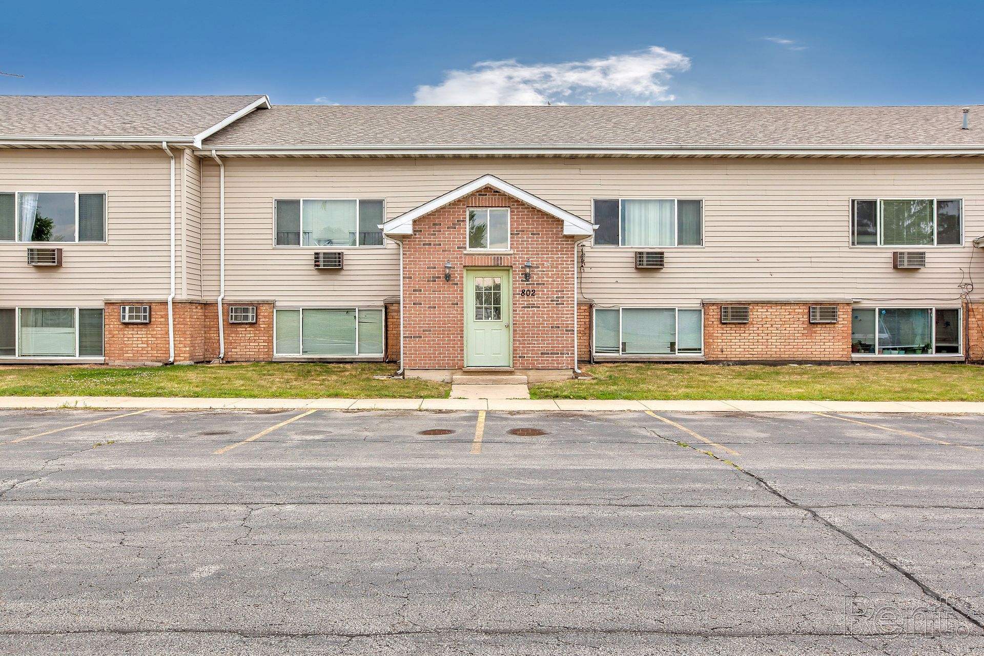 Two-story beige apartment building with a brick facade and a parking lot in front.