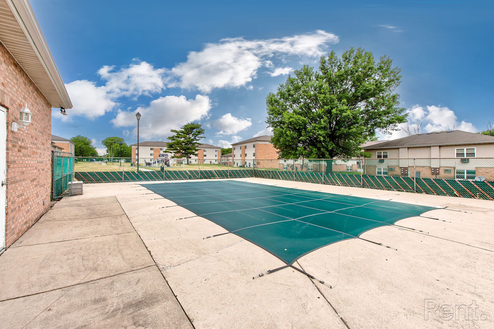 Pool covered with green tarp in residential area, blue sky with clouds.
