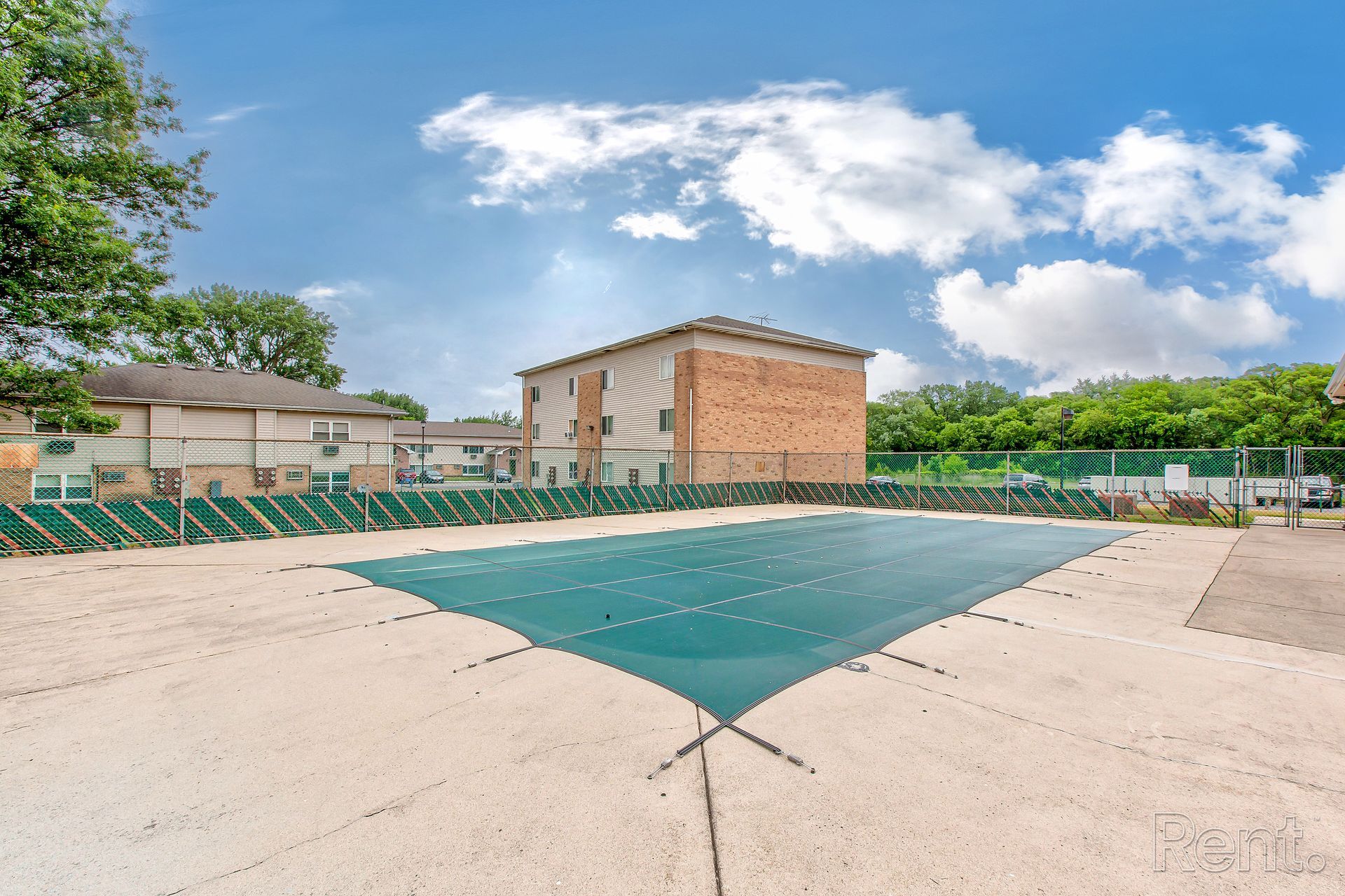 A pool covered in green netting, with a brick building in the background under a blue sky.