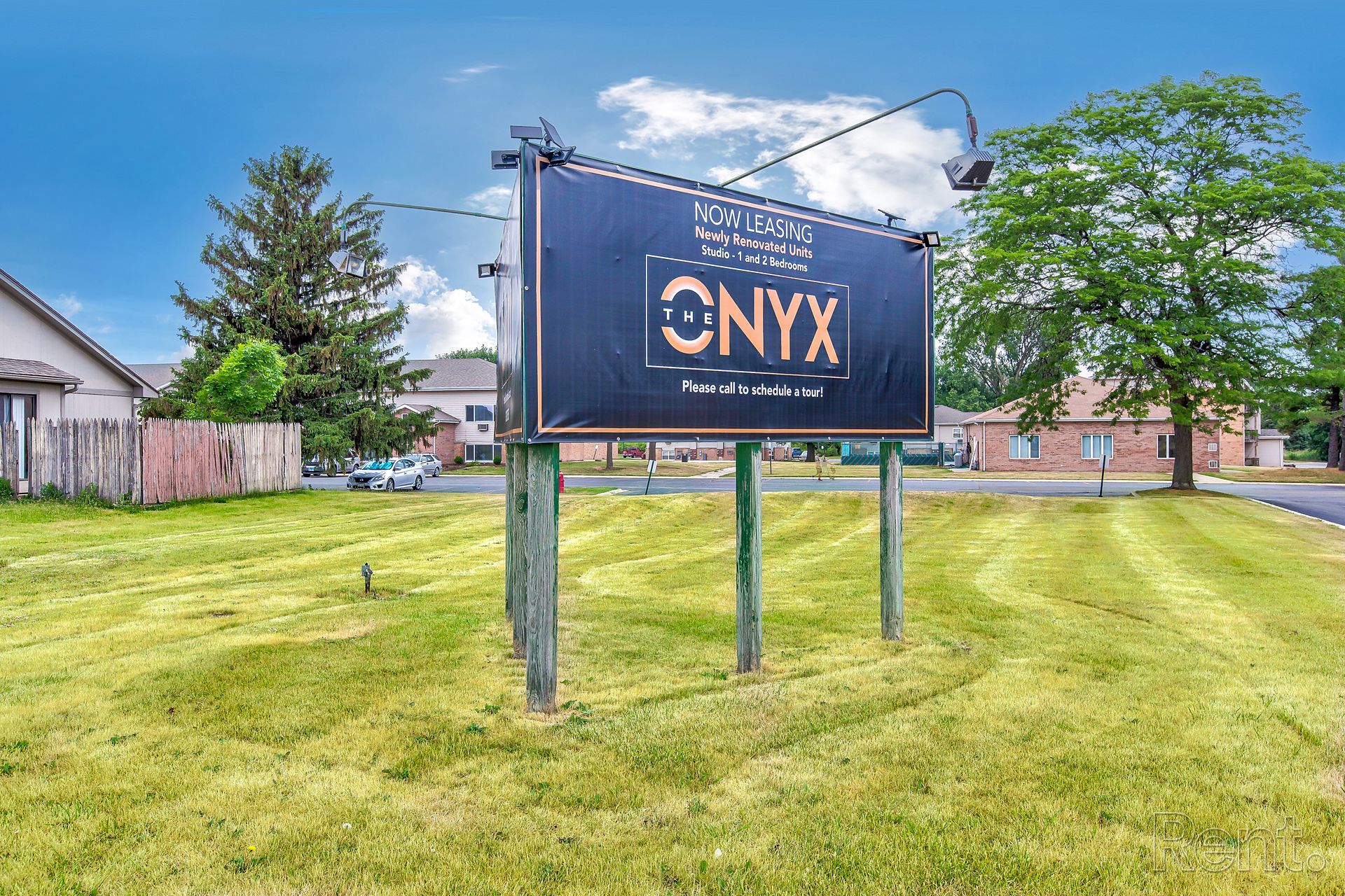 Sign for Onyx Apartments in grassy area, with blue sky and buildings in background.